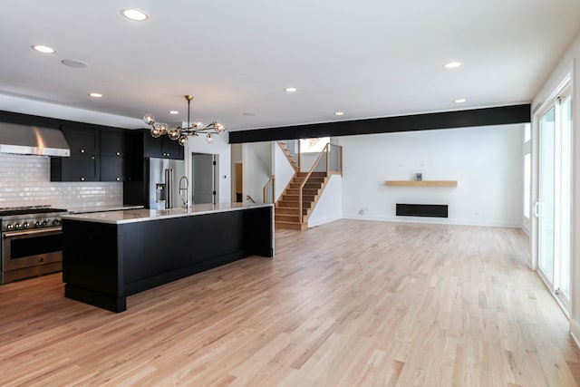 kitchen featuring wall chimney range hood, decorative light fixtures, light hardwood / wood-style floors, high end appliances, and a kitchen island with sink