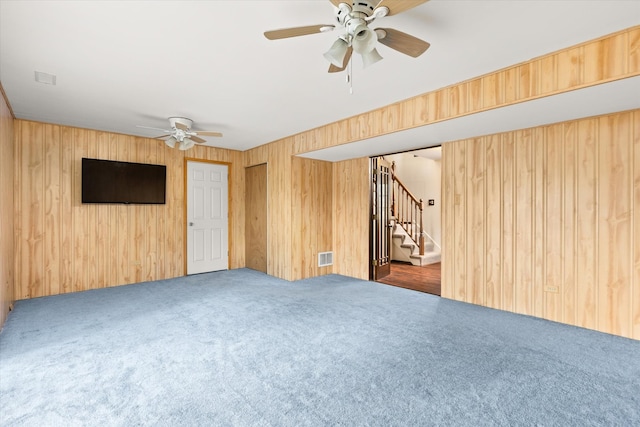 carpeted empty room featuring wood walls and ceiling fan