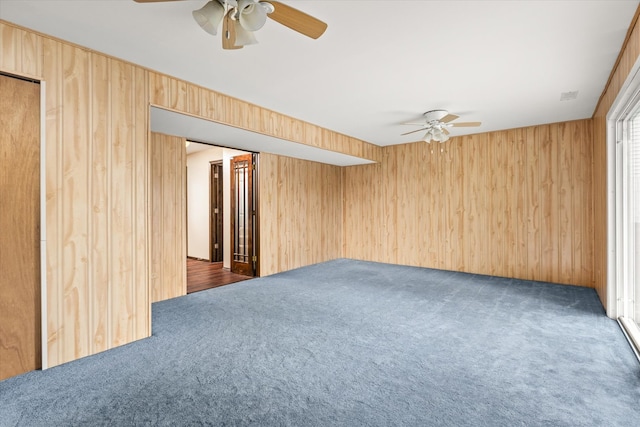 empty room featuring wooden walls, ceiling fan, and dark carpet