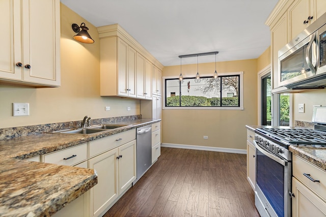 kitchen with sink, appliances with stainless steel finishes, dark hardwood / wood-style floors, cream cabinetry, and pendant lighting