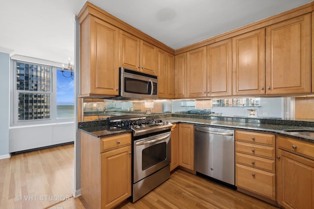 kitchen featuring appliances with stainless steel finishes, backsplash, light hardwood / wood-style flooring, and dark stone countertops