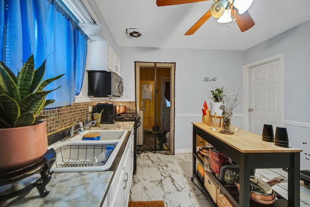 kitchen featuring backsplash, sink, white gas range oven, ceiling fan, and white cabinetry