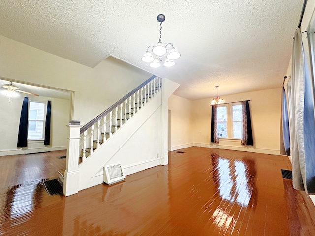 unfurnished living room with hardwood / wood-style floors, ceiling fan with notable chandelier, and a textured ceiling