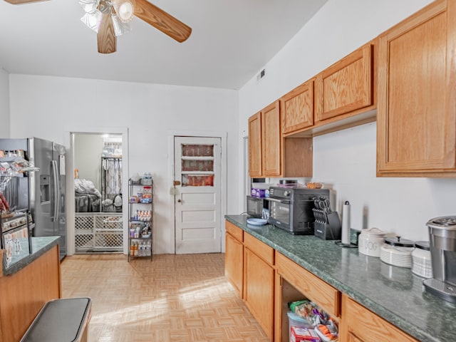 kitchen with dark stone countertops, light parquet flooring, stainless steel refrigerator with ice dispenser, and ceiling fan