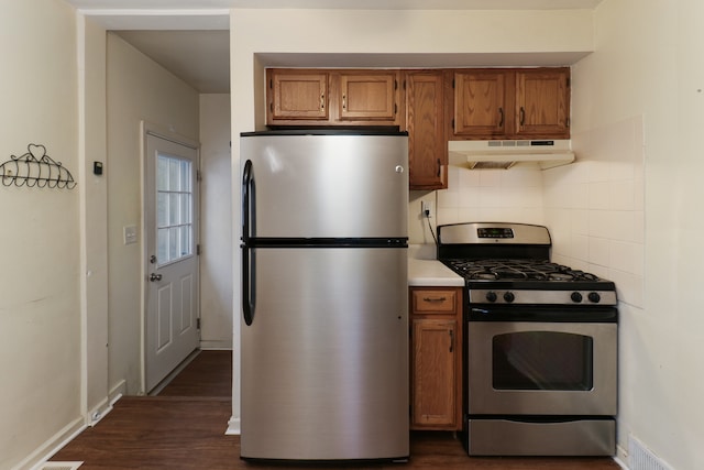 kitchen with appliances with stainless steel finishes, dark wood-type flooring, and tasteful backsplash