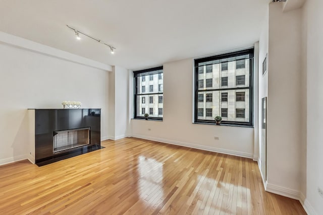 unfurnished living room featuring rail lighting, a fireplace with flush hearth, baseboards, and light wood-style flooring