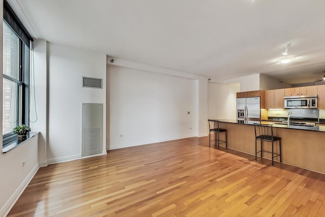 kitchen with stainless steel appliances, visible vents, light wood-style floors, a kitchen breakfast bar, and dark countertops