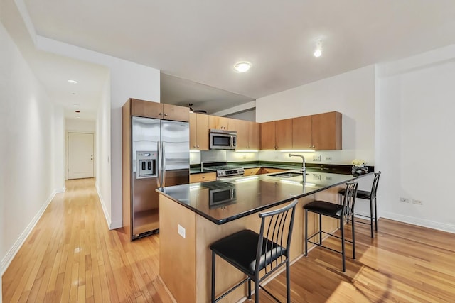 kitchen with dark countertops, appliances with stainless steel finishes, a sink, light wood-type flooring, and a kitchen bar