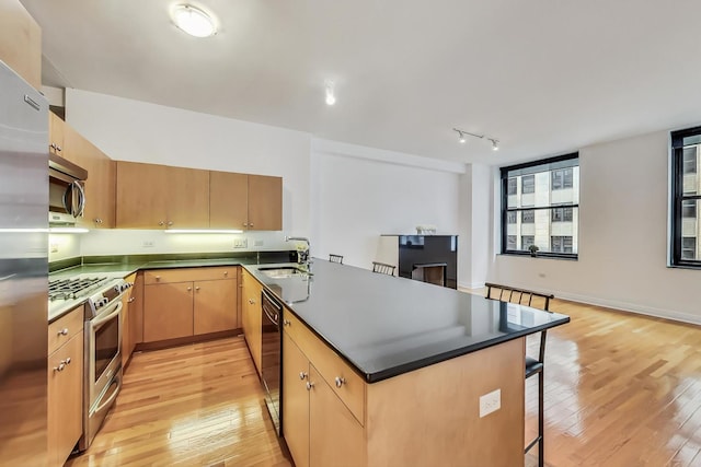 kitchen featuring appliances with stainless steel finishes, light wood-style floors, a sink, a peninsula, and a kitchen breakfast bar