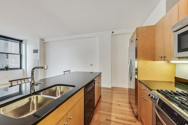 kitchen with a sink, visible vents, appliances with stainless steel finishes, light wood-type flooring, and dark countertops