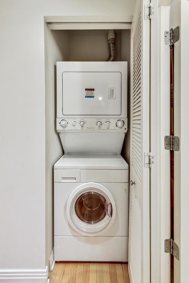 laundry area with stacked washer and dryer, light wood-type flooring, laundry area, and baseboards