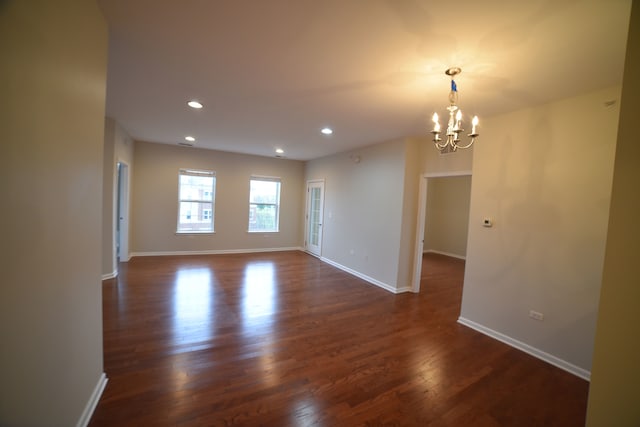 empty room with dark hardwood / wood-style flooring and an inviting chandelier