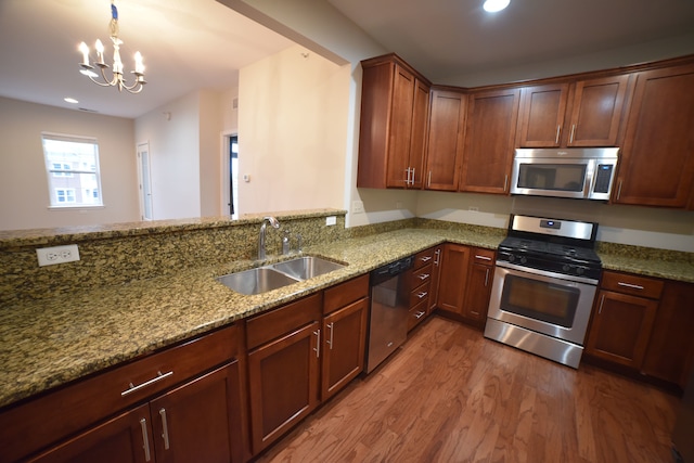 kitchen featuring wood-type flooring, light stone counters, stainless steel appliances, an inviting chandelier, and sink