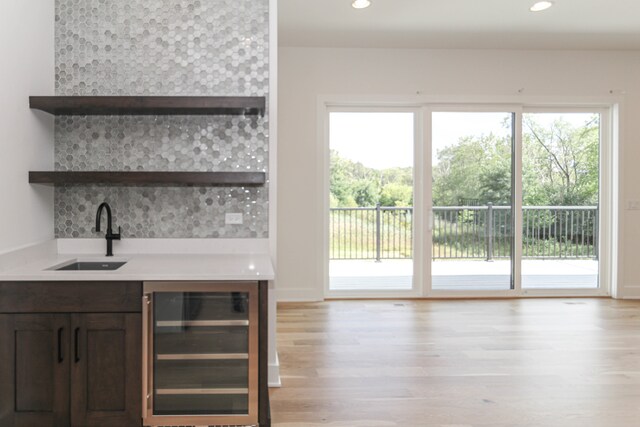 bar featuring dark brown cabinetry, sink, beverage cooler, light hardwood / wood-style flooring, and decorative backsplash