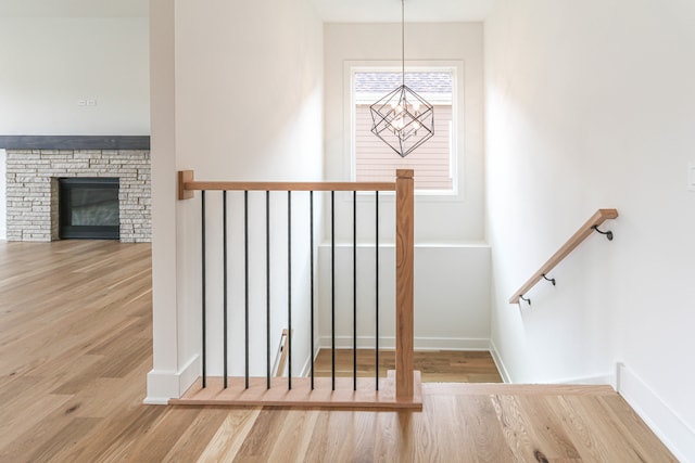 stairway featuring a stone fireplace, hardwood / wood-style floors, and a notable chandelier