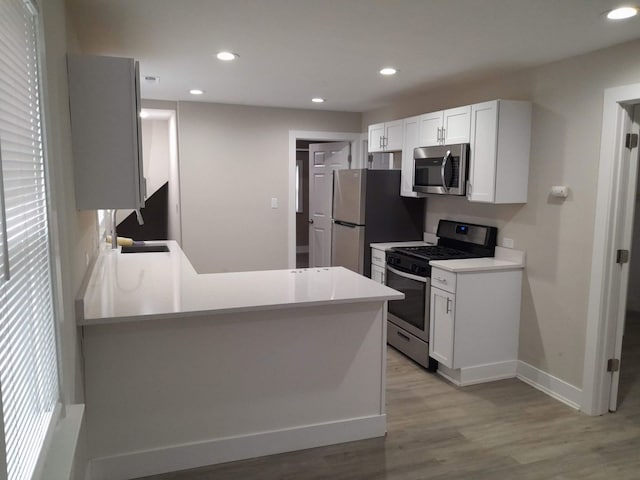 kitchen featuring kitchen peninsula, white cabinets, light hardwood / wood-style floors, and stainless steel appliances