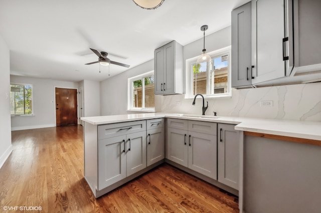 kitchen featuring sink, kitchen peninsula, dark wood-type flooring, gray cabinetry, and pendant lighting