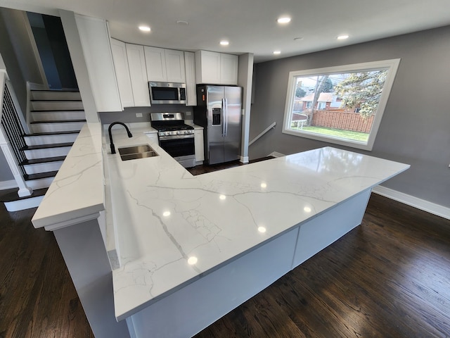 kitchen featuring appliances with stainless steel finishes, light stone countertops, sink, white cabinets, and kitchen peninsula