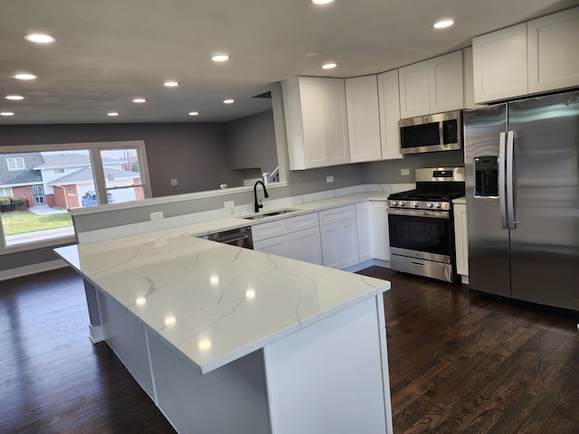 kitchen with sink, kitchen peninsula, light stone counters, appliances with stainless steel finishes, and white cabinets