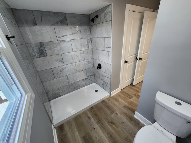 bathroom with toilet, hardwood / wood-style floors, and a tile shower