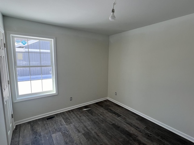 spare room with dark wood-style floors, visible vents, a wealth of natural light, and baseboards