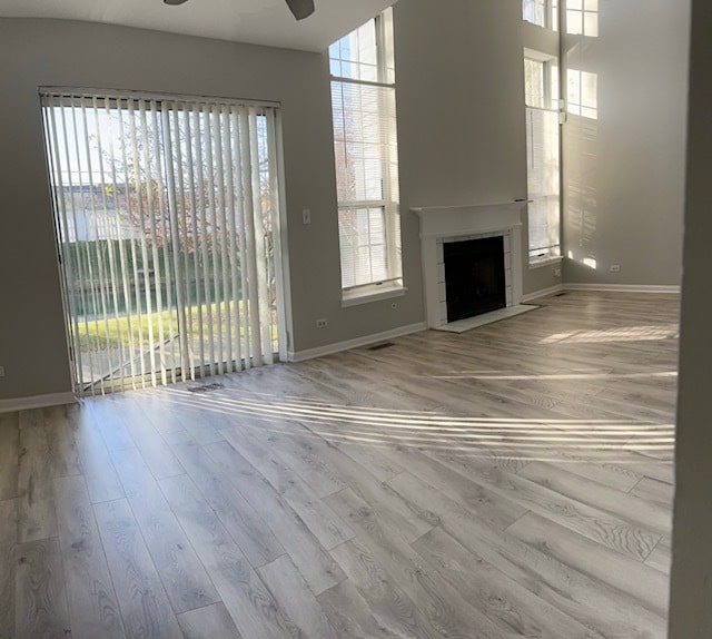 unfurnished living room featuring a fireplace, ceiling fan, plenty of natural light, and light hardwood / wood-style floors