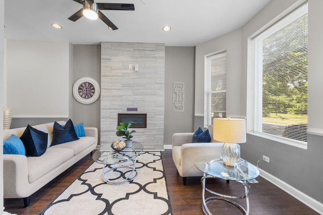 living room with ceiling fan, a tiled fireplace, and dark hardwood / wood-style flooring