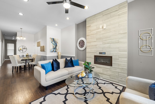 living room featuring dark wood-type flooring, a tiled fireplace, and ceiling fan with notable chandelier