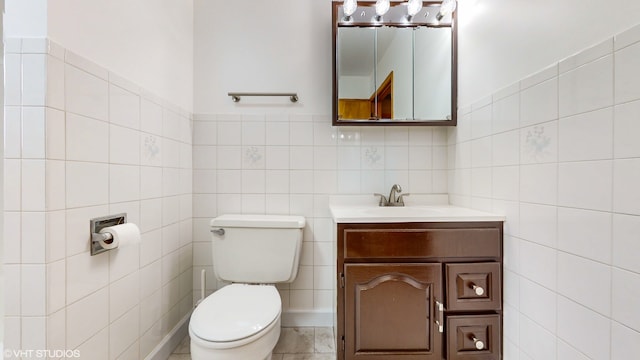 bathroom with toilet, vanity, tile walls, and tile patterned flooring