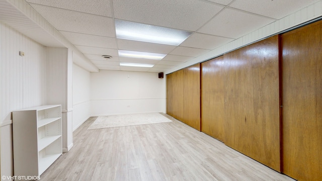 basement with light hardwood / wood-style flooring, a paneled ceiling, and wooden walls