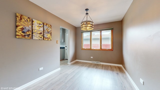 spare room with an inviting chandelier and light hardwood / wood-style flooring