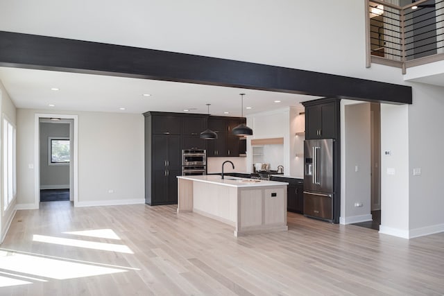 kitchen with light hardwood / wood-style floors, sink, appliances with stainless steel finishes, an island with sink, and pendant lighting