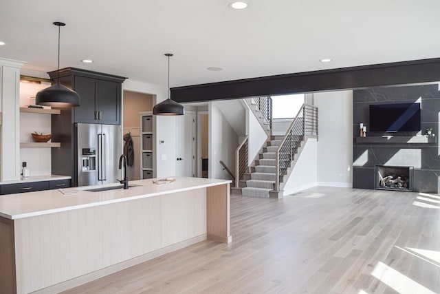 kitchen featuring high quality fridge, a center island with sink, pendant lighting, and light hardwood / wood-style flooring