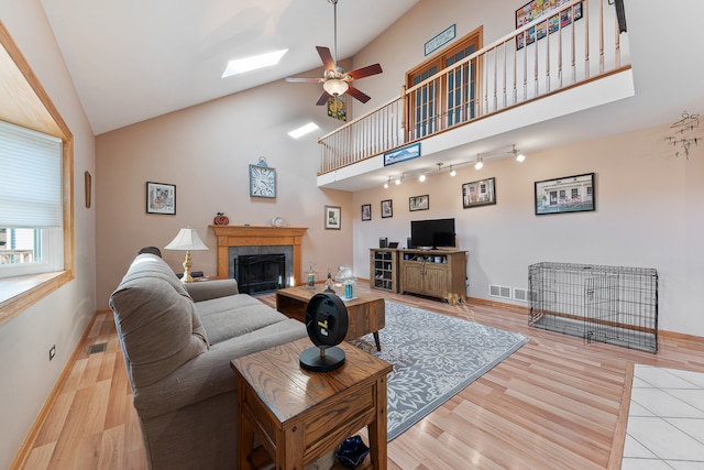 living room featuring ceiling fan, light hardwood / wood-style floors, high vaulted ceiling, and a skylight