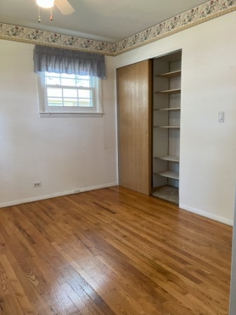 unfurnished bedroom featuring hardwood / wood-style flooring, ceiling fan, and a closet