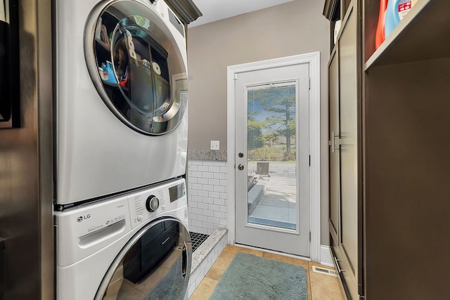 clothes washing area featuring light tile patterned floors, laundry area, visible vents, and stacked washer / drying machine