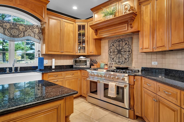 kitchen featuring dark stone counters, a sink, double oven range, backsplash, and light tile patterned flooring