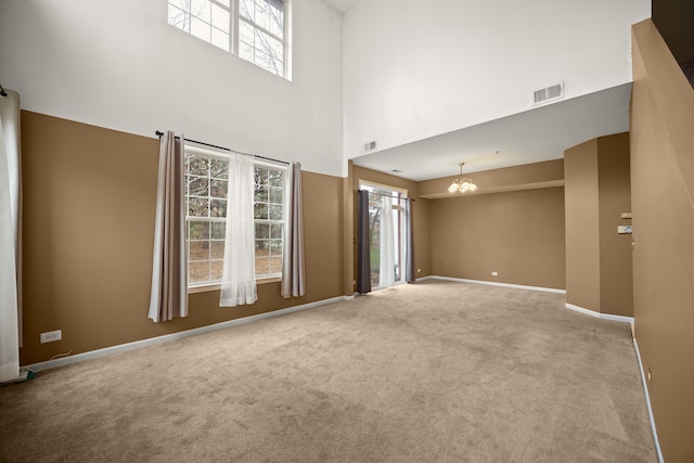 carpeted spare room featuring a wealth of natural light, a high ceiling, and a chandelier