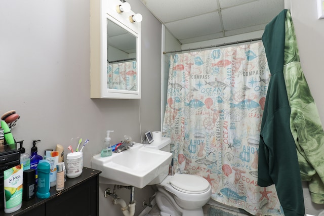 bathroom with walk in shower, a paneled ceiling, toilet, and sink