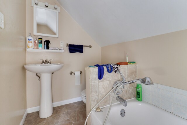 bathroom featuring lofted ceiling, a tub to relax in, toilet, and sink