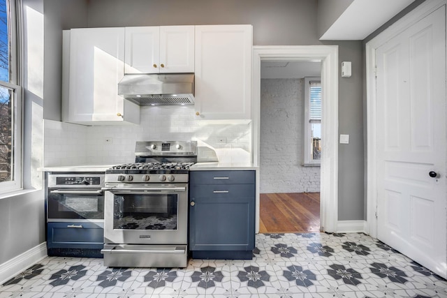 kitchen featuring blue cabinetry, wall chimney range hood, backsplash, white cabinets, and stainless steel range with gas stovetop