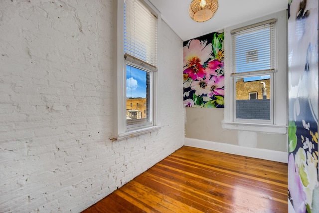 unfurnished room featuring hardwood / wood-style floors and brick wall