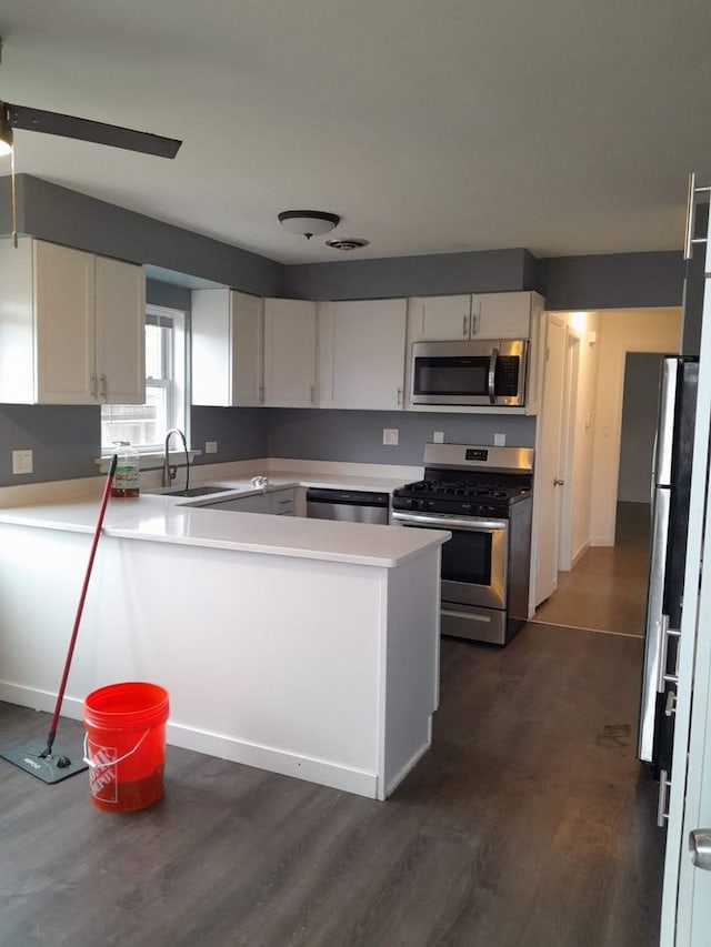 kitchen with stainless steel appliances, dark wood-type flooring, kitchen peninsula, sink, and white cabinetry