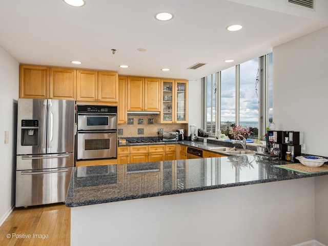 kitchen with dark stone counters, appliances with stainless steel finishes, sink, light hardwood / wood-style floors, and kitchen peninsula