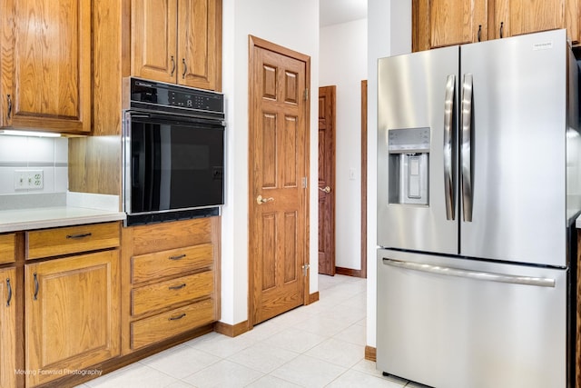 kitchen with stainless steel fridge with ice dispenser, light tile patterned floors, black oven, and backsplash