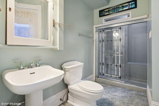 bathroom featuring a shower with shower door, sink, and toilet