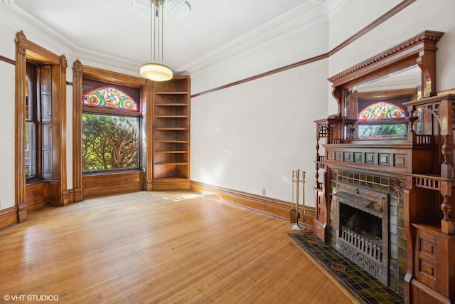 unfurnished living room with built in shelves, ornamental molding, a tiled fireplace, and light hardwood / wood-style flooring