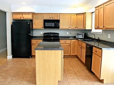 kitchen with black appliances, light brown cabinetry, sink, and a center island