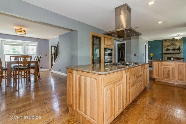 kitchen featuring island exhaust hood, a fireplace, appliances with stainless steel finishes, light brown cabinets, and light hardwood / wood-style floors