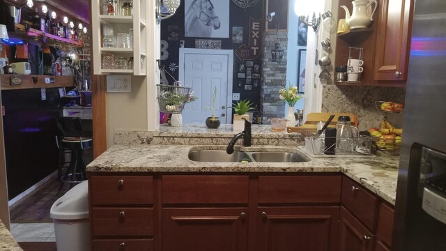 kitchen featuring backsplash, light stone counters, stainless steel refrigerator, and sink